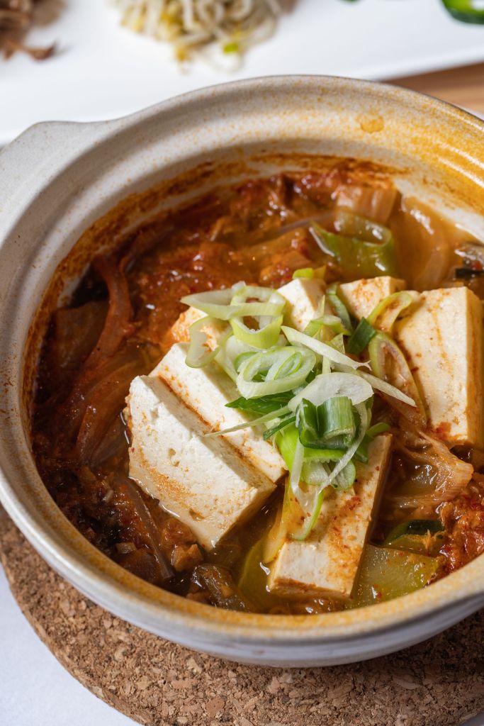 Korean kimchi jjigae stew with tofu and vegetables bubbling in a clay pot