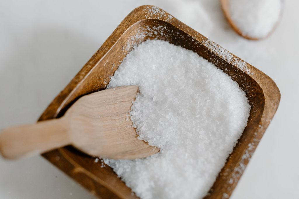 Coarse sea salt crystals in a wooden bowl with a wooden scoop