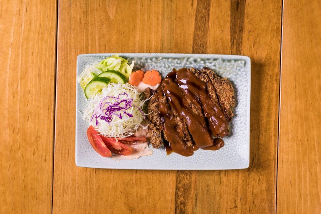 Crispy Korean-style pork cutlet (donkkaseu) with fresh vegetables on a ceramic plate
