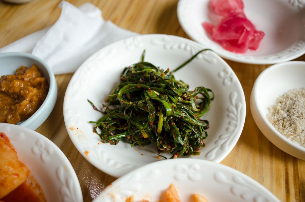 Assorted Korean side dishes including seasoned seaweed in white bowls on a wooden table
