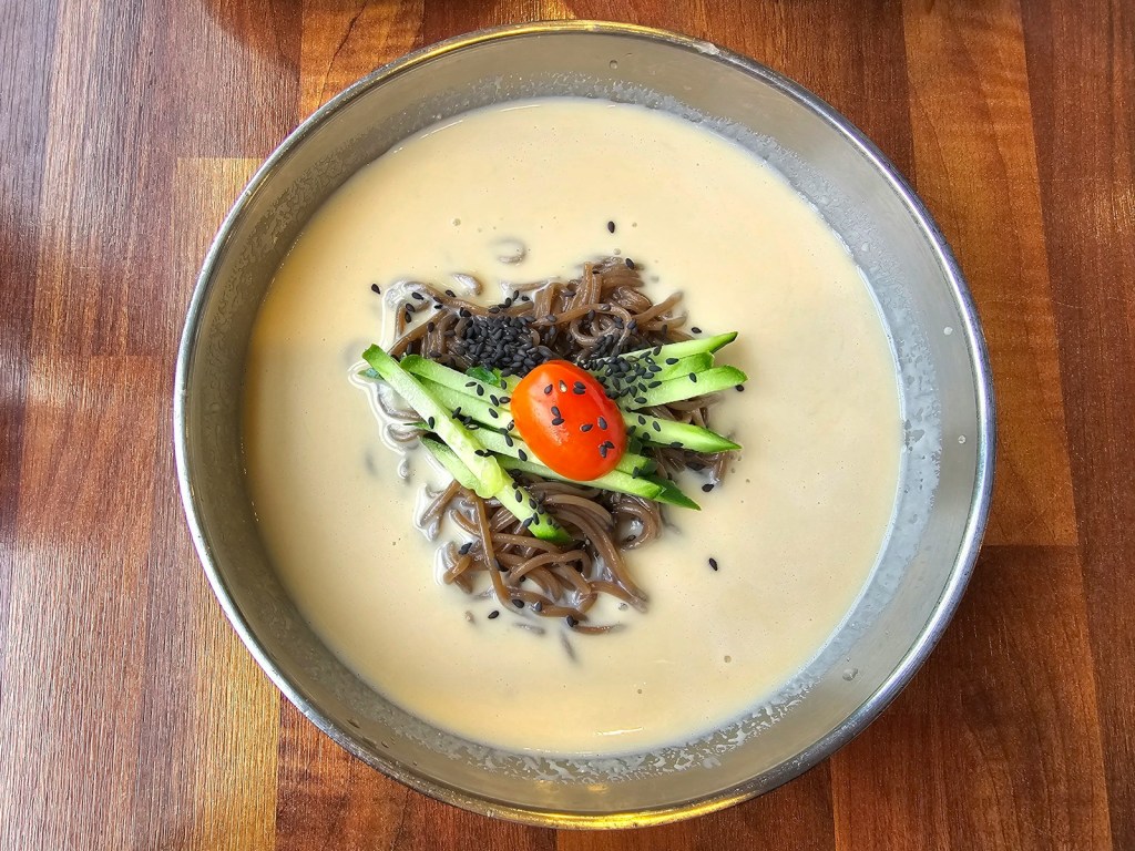 Bowl of Korean cold soybean noodle soup on a wooden table