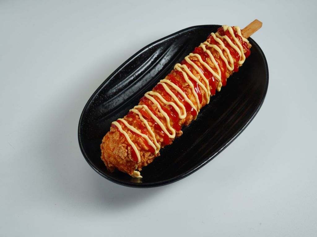 Crispy Korean corn dog on a stick topped with ketchup and mustard