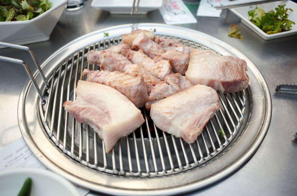 Pork pieces cooking on a Korean barbecue grill with side dishes nearby