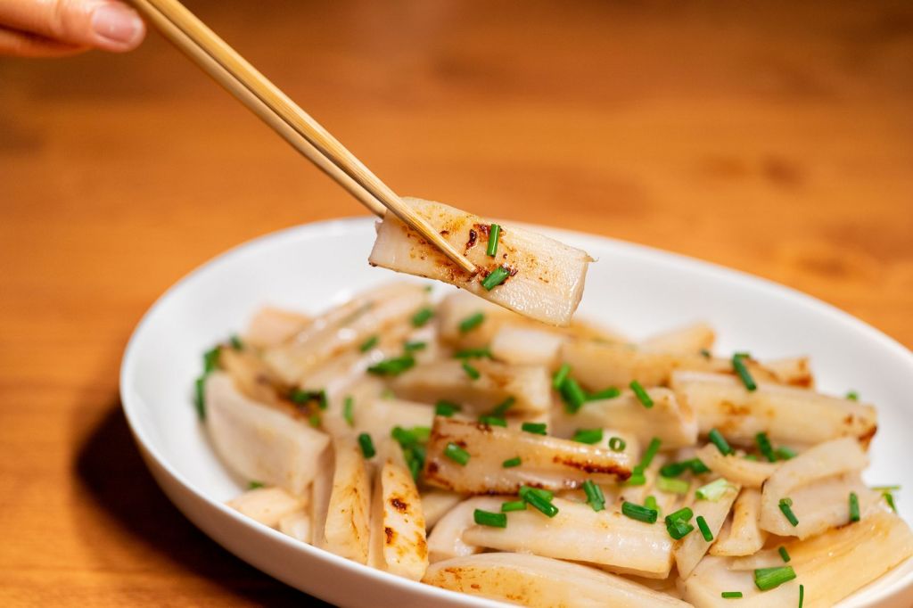 Chopsticks lifting a Korean rice cake from a dish garnished with fresh chives