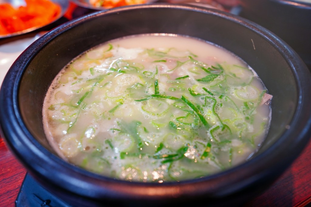 Steaming bowl of clear Korean soup topped with sliced green onions