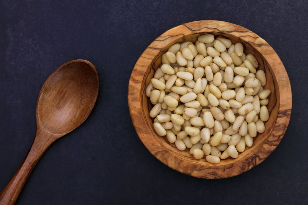 Shelled pine nuts in a wooden bowl next to a spoon, the base of Korean pine nut sauce