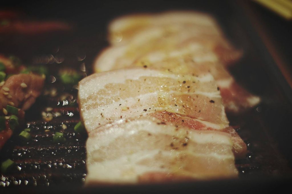 Slices of marinated pork grilling on a barbecue grill with peppers