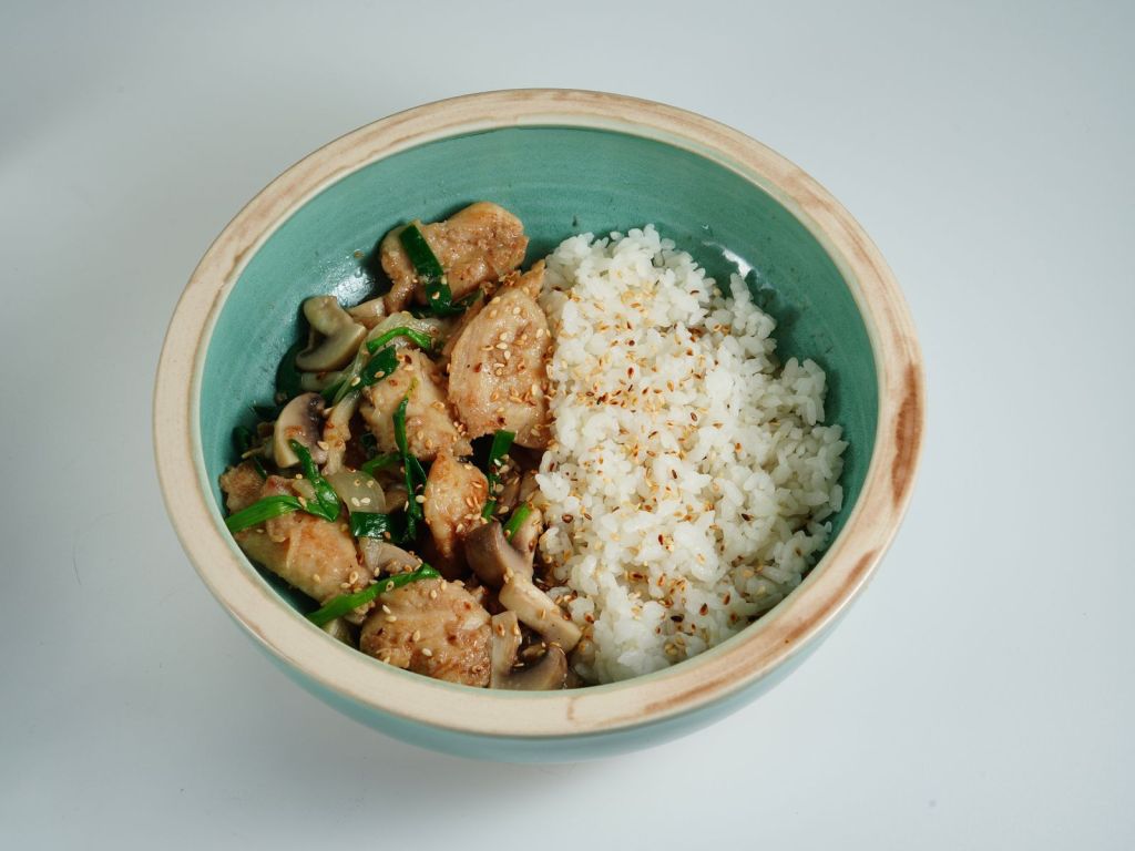 Soy-glazed stir-fried chicken served over rice in a ceramic bowl