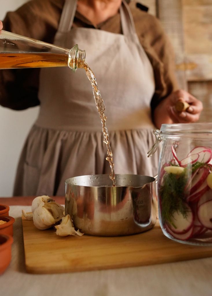 Vinegar being poured into a jar of vegetables for homemade pickles