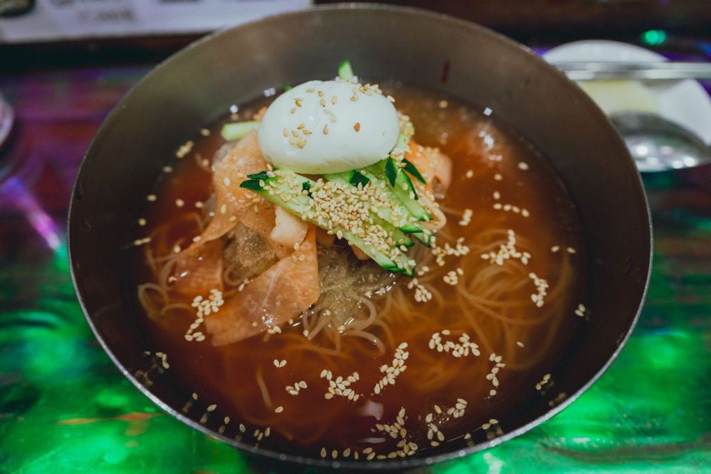 Bowl of Korean cold noodles (mul naengmyeon) with egg, cucumber and sesame seeds, a dish traditionally seasoned with gyeoja mustard