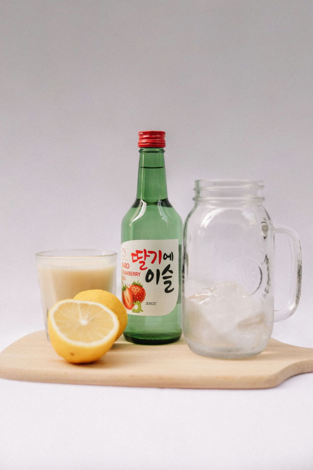 Green soju bottle beside a pitcher of milky drink, lemon and an ice-filled glass
