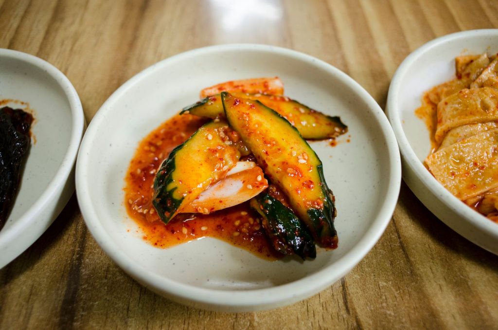 Spicy Korean cucumber kimchi in a white ceramic bowl on a wooden table