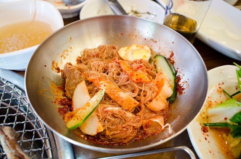Spicy Korean chewy noodles tossed in red chili sauce with sliced vegetables and kimchi