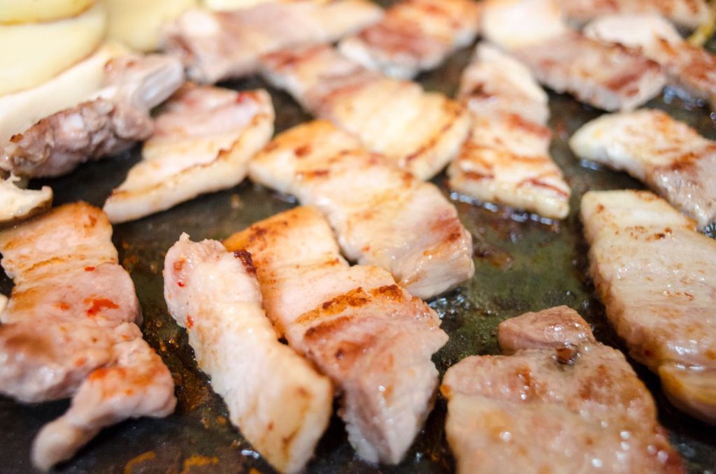 Korean pork belly slices sizzling on a hot grill