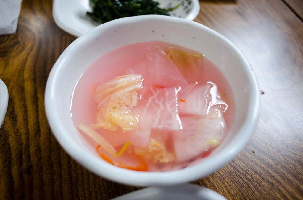 Korean pink radish water kimchi in a white bowl on a wooden table
