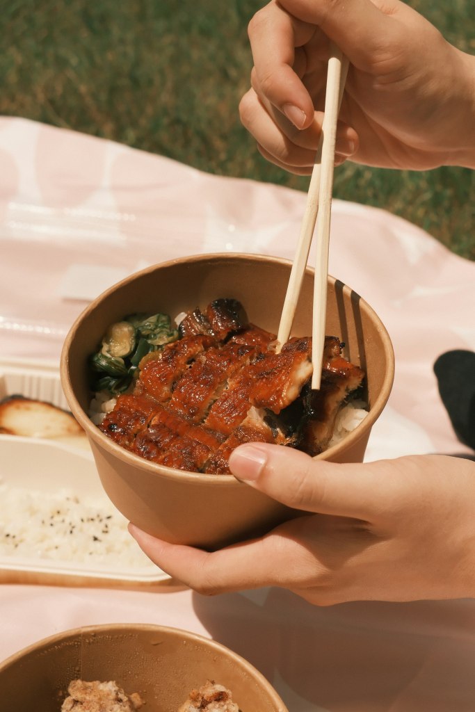 Bowl of glazed grilled eel over rice held with chopsticks