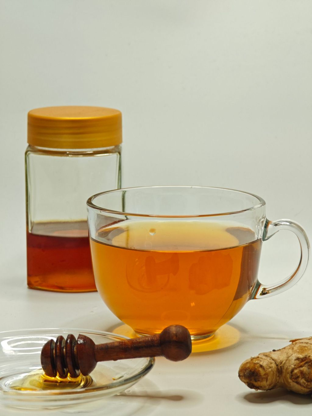 Glass cup of warm ginger tea beside a honey jar and fresh ginger root