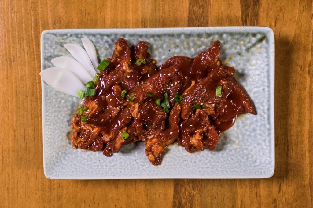 Glazed Korean grilled beef topped with green onions on a ceramic plate